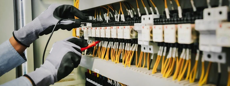 Elektrikář měří napětí v rozvaděči s žlutými kabely.