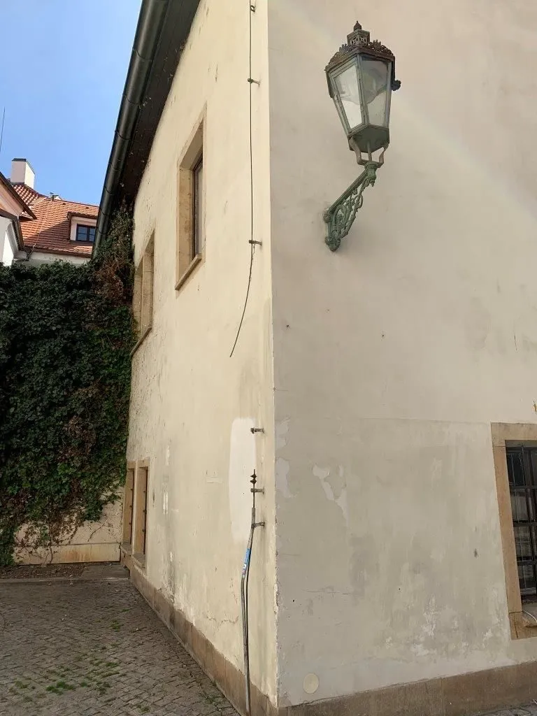 Bílá fasáda budovy s hromosvodem na stěně.