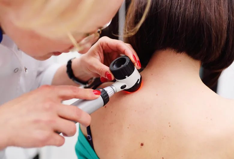 Dermatolog zkoumá znaménko na zádech pacienta pomocí daskopu.