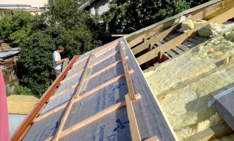 Stavebník montuje trámy na střechu s izolací při rekonstrukci.