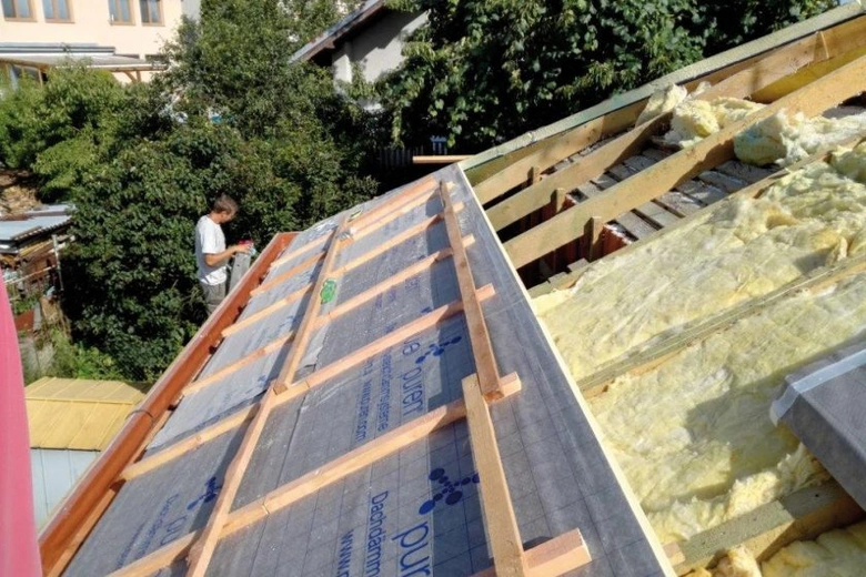 Stavebník montuje trámy na střechu s izolací při rekonstrukci.
