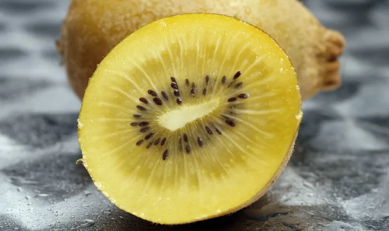 Žlutý řezaný kiwi s černými semínky na šedém povrchu.