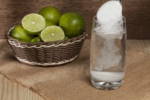 Sklenice s bublající vodou, do které se přidává jedlá soda vedle košíku limet.