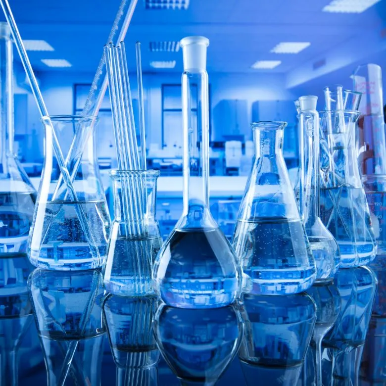 Skleněná laboratorní nádobí s tekutinami v modrém osvětlení.