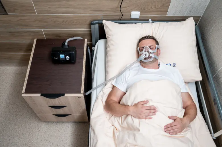 Muž spí v posteli s přístrojem na dýchání CPAP.