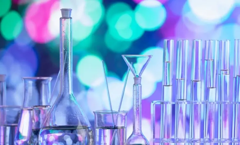 Laboratorní sklo s tekutinami na barevném pozadí.