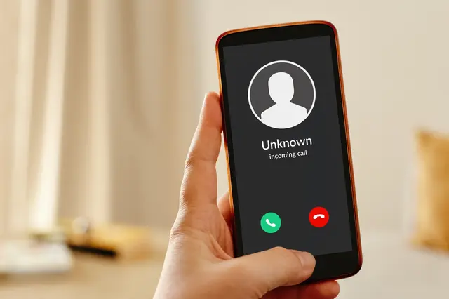 Ruka drží telefon s příchozím voláním od neznámého.