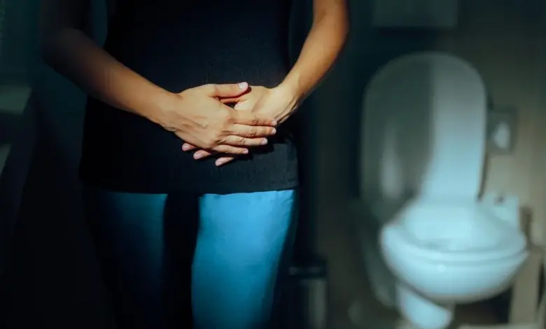 Žena drží břicho v koupelně kvůli nutkání na močení.