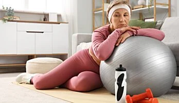 Žena v sportovním oblečení sedí na podlaze s fitness kouli.