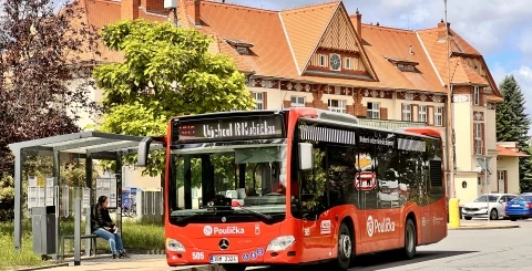 Červený autobus v Uherském Hradišti u zastávky s historickými domy.