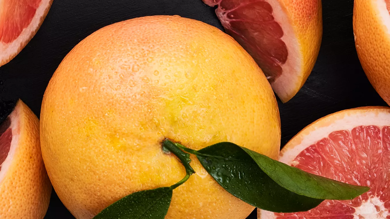 Celý pomelo s listy a řezané plátky na tmavém pozadí.